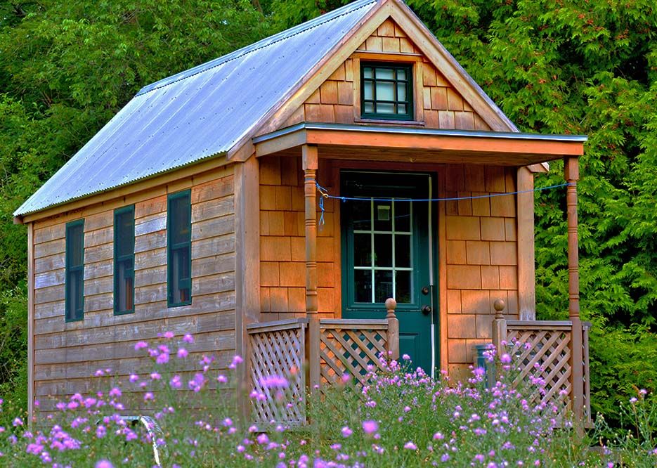 Zu sehen ist ein Tiny House, welches von Blumen die blühen, umringt wird.